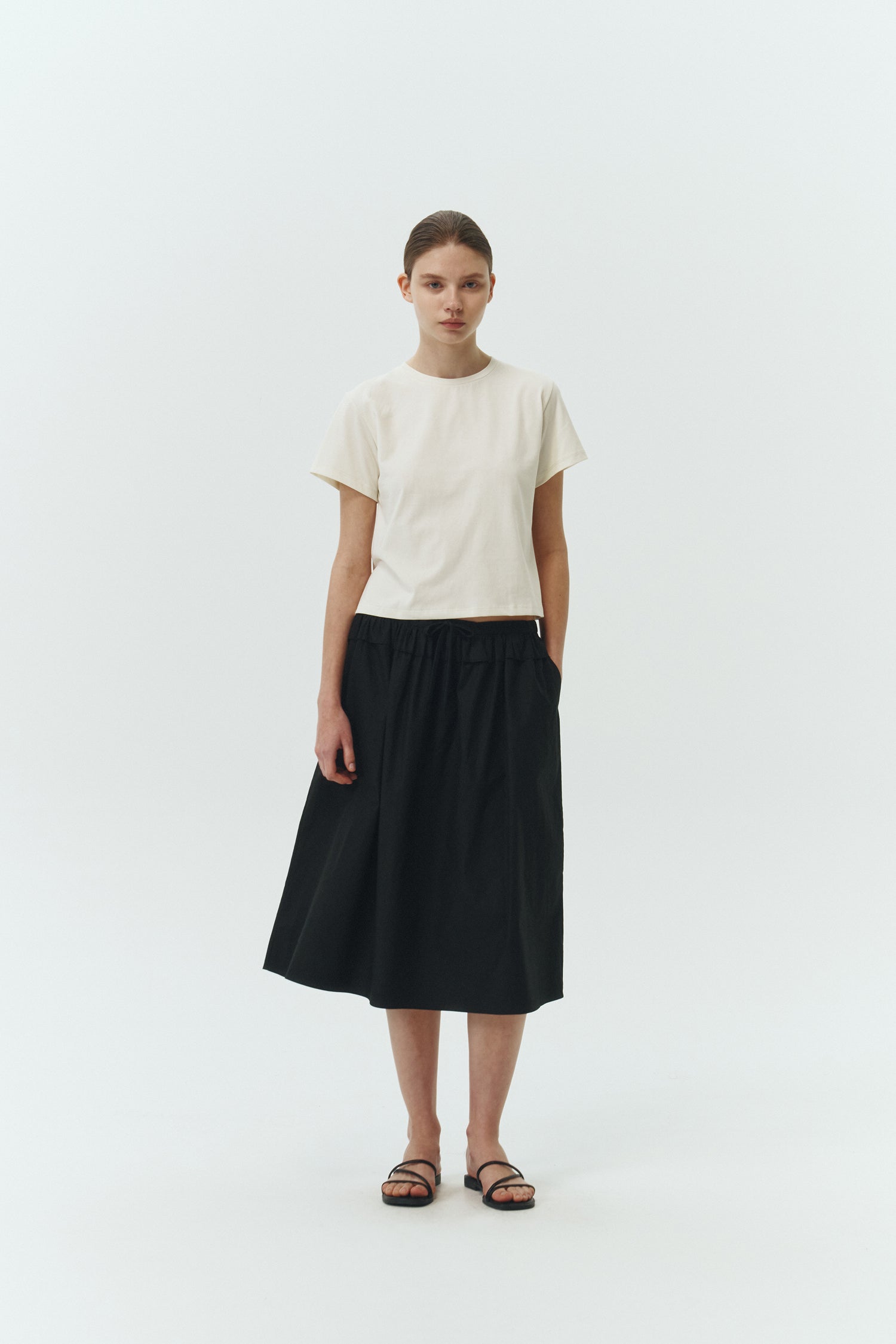 Maryam Skirt in black, a midi cotton skirt with shirred waistband, drawstring detail, side pockets, and a softly flared silhouette