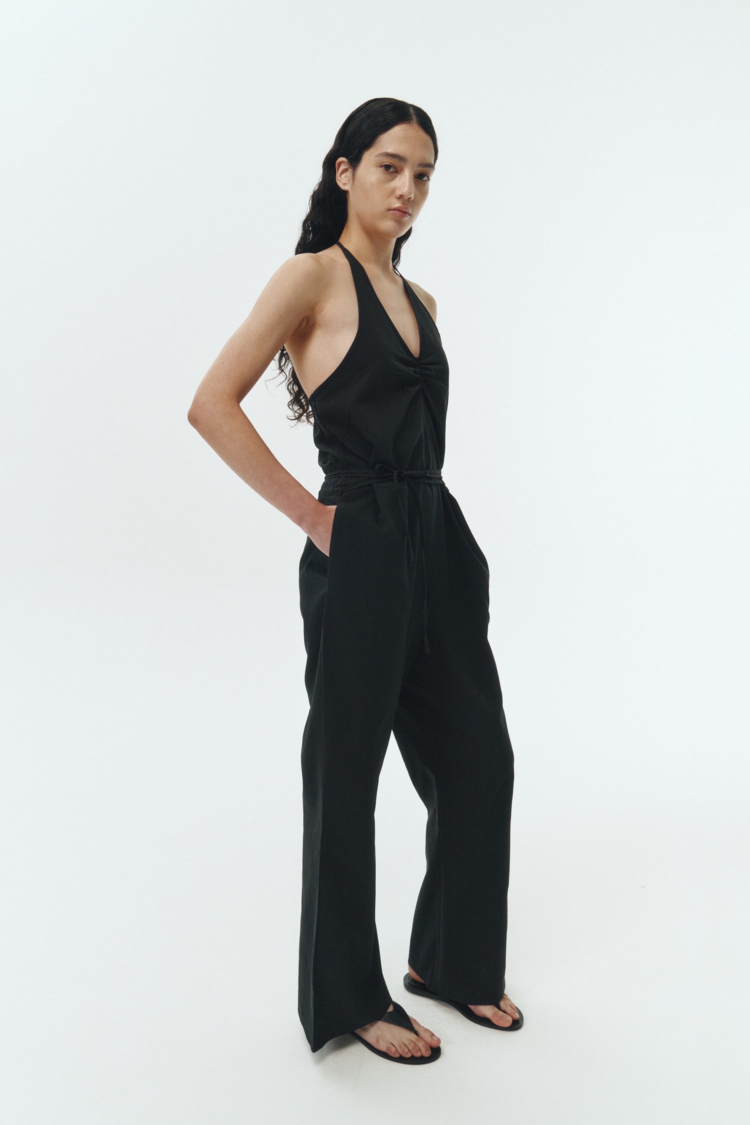 Daisy Jumpsuit in black, sleeveless linen blend jumpsuit with adjustable halterneck, open back, straight-leg silhouette, and relaxed fit.