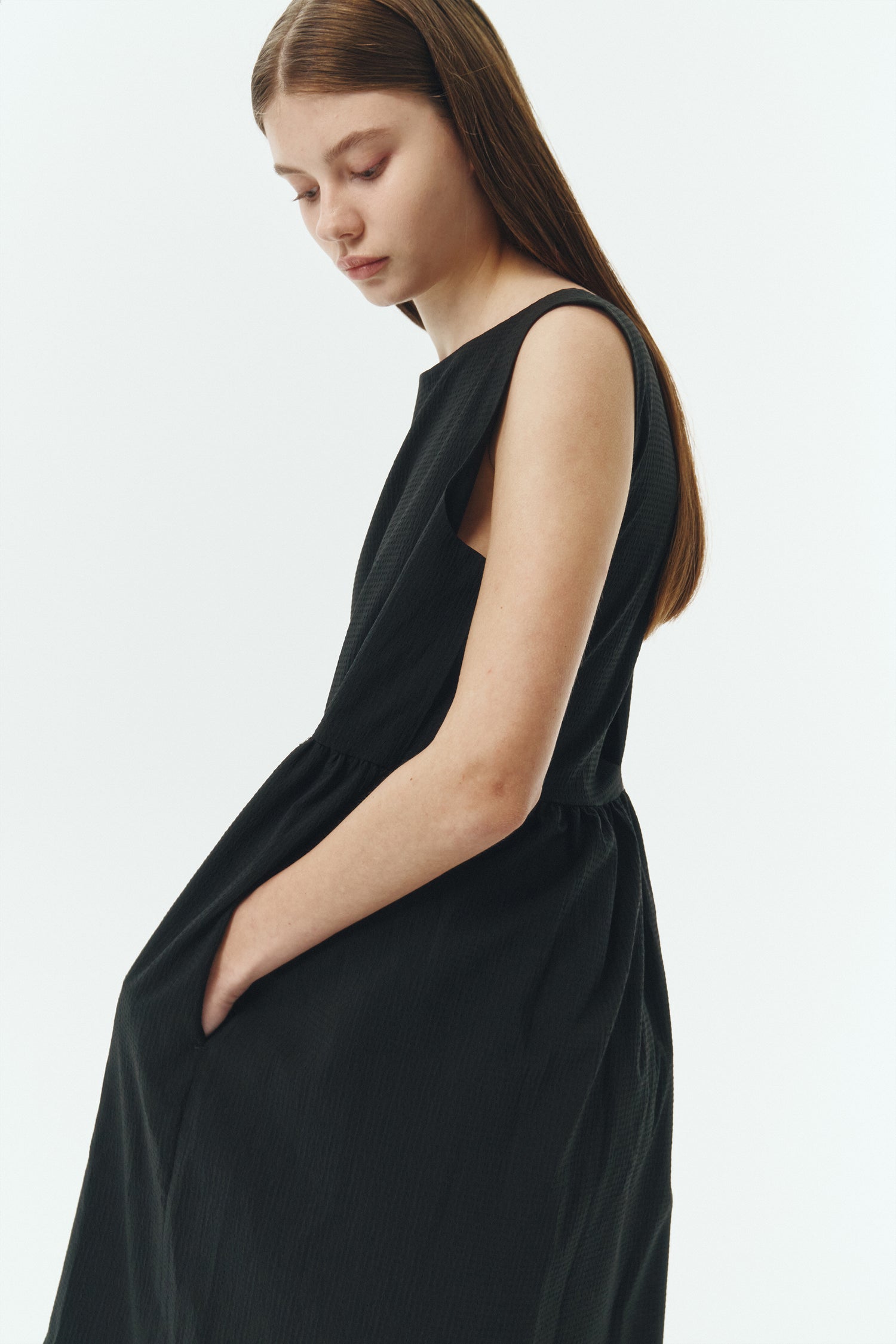 Pina Dress in black, sleeveless cotton midi dress with shirring at waist and hem, hidden side pockets, and an open back with button closure.