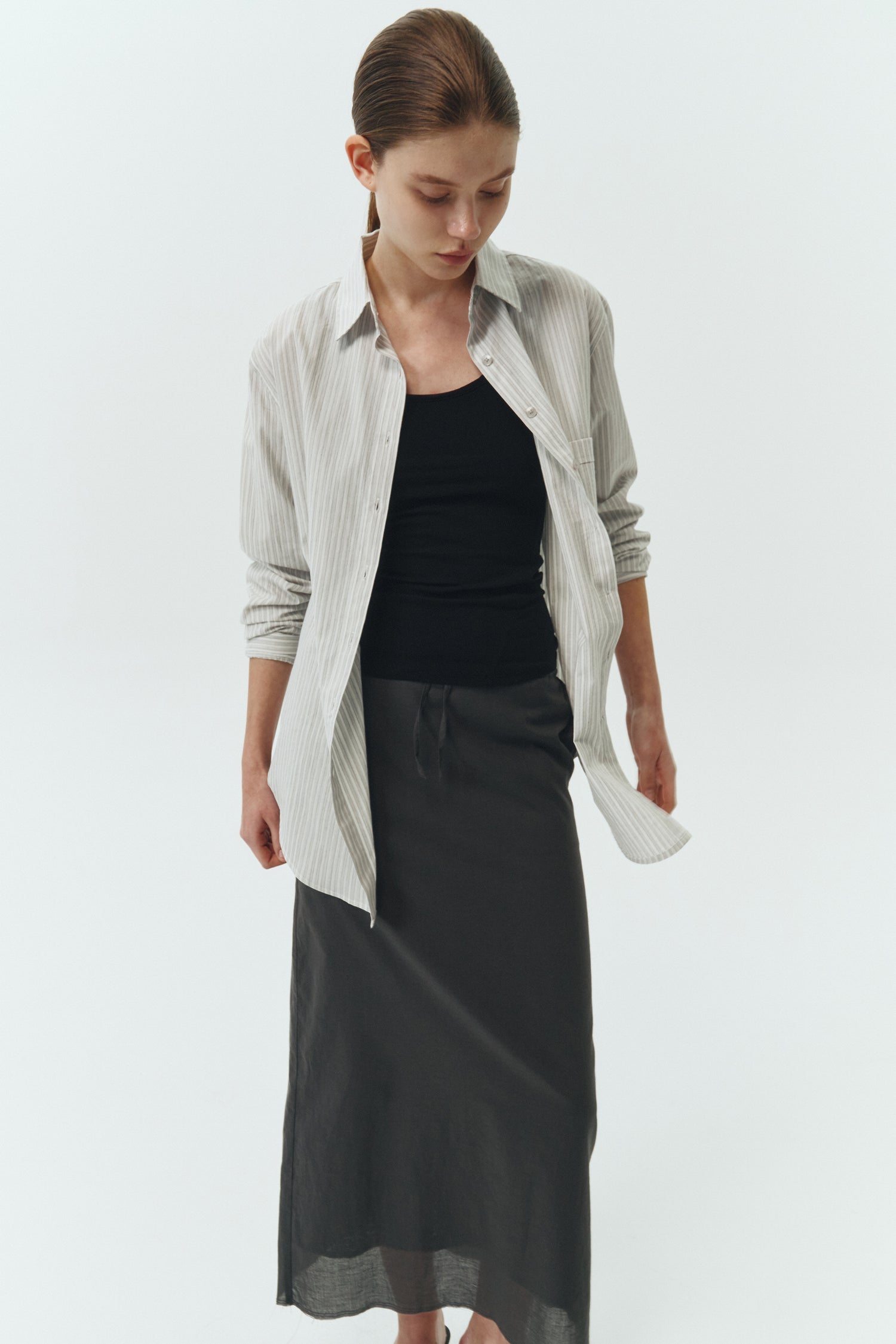 Amelia Skirt in charcoal, a lightweight cotton midi skirt with inner drawstring waist, hidden side pockets, lined layers, raw-edge hem, and a center back slit for ease and movement