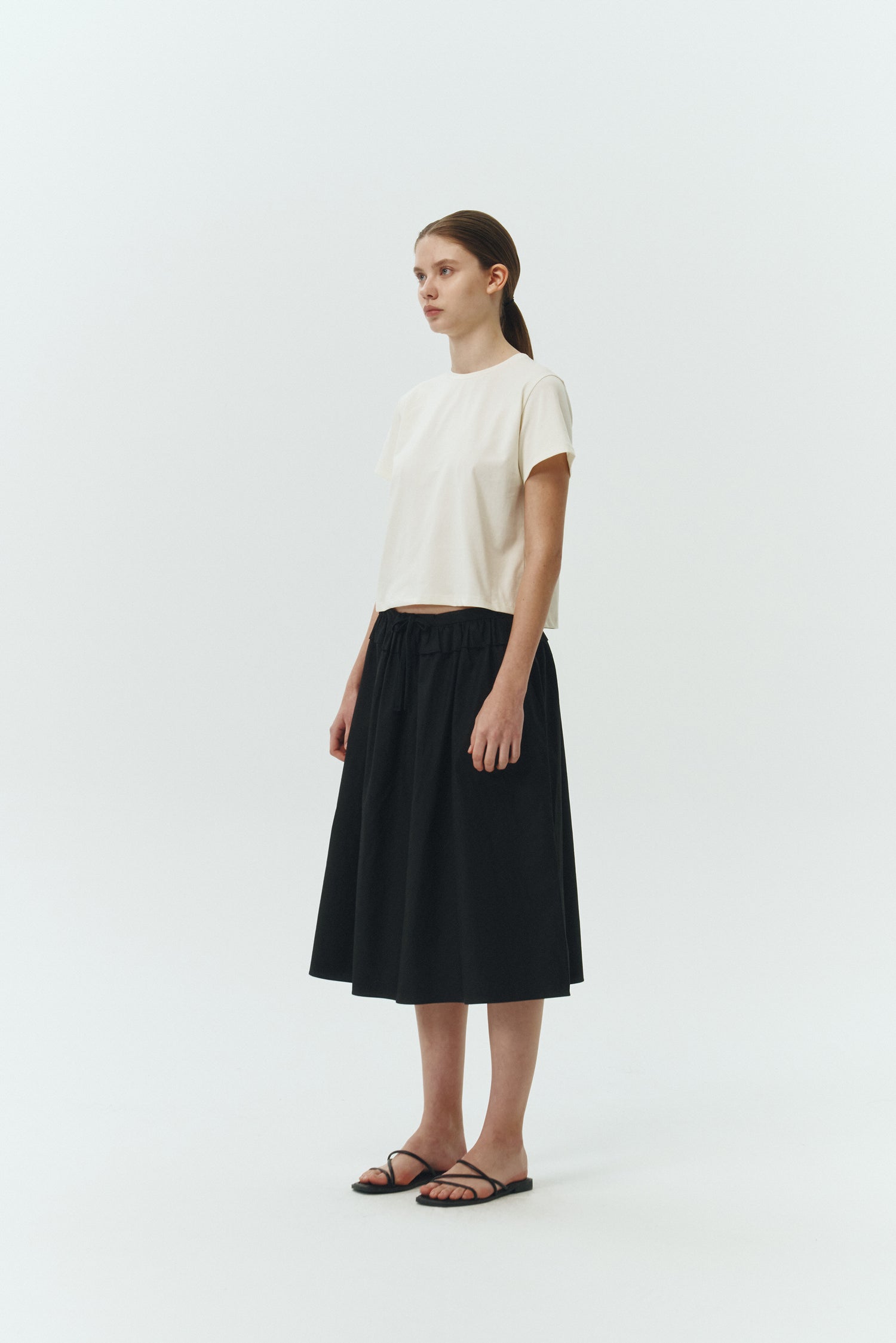 Maryam Skirt in black, a midi cotton skirt with shirred waistband, drawstring detail, side pockets, and a softly flared silhouette