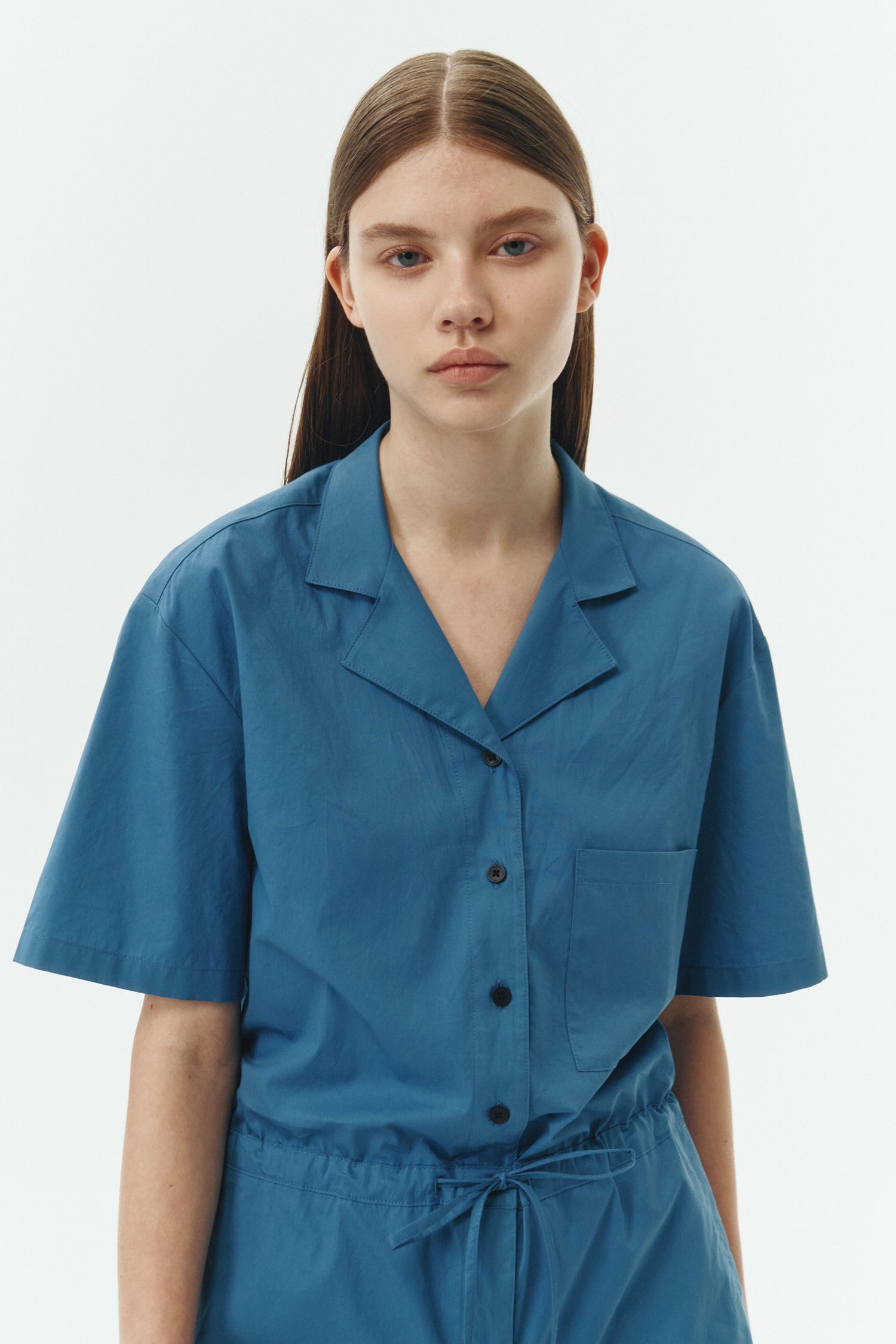 Emma Jumpsuit in blue green, short-sleeve cotton jumpsuit with camp collar, front buttons, drawstring waist, and multiple pockets.