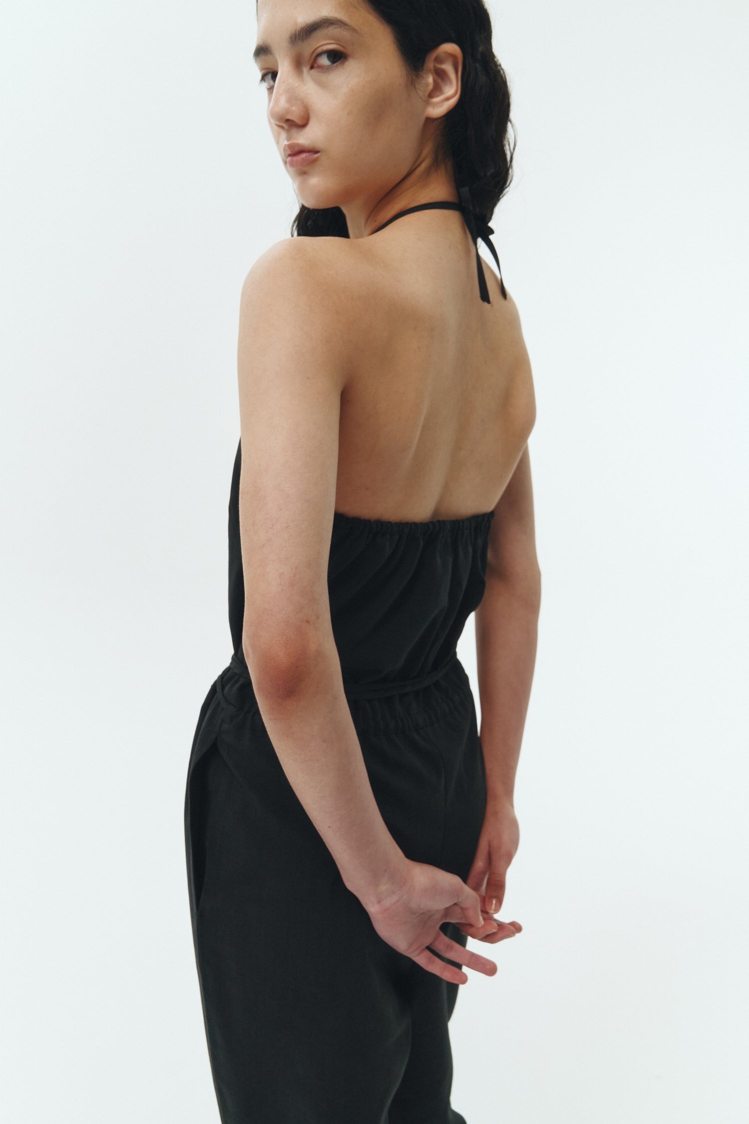 Daisy Jumpsuit in black, sleeveless linen blend jumpsuit with adjustable halterneck, open back, straight-leg silhouette, and relaxed fit.