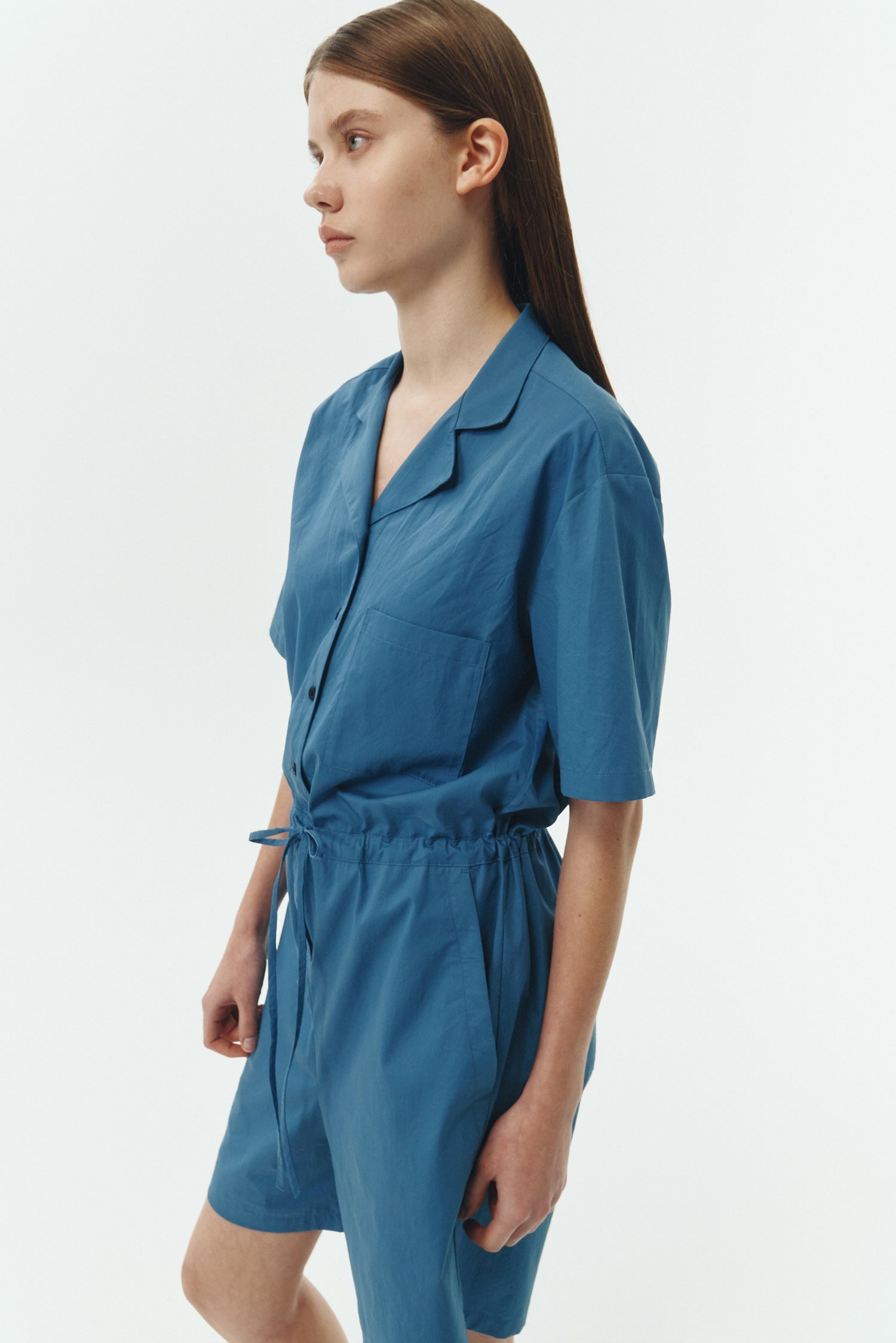 Emma Jumpsuit in blue green, short-sleeve cotton jumpsuit with camp collar, front buttons, drawstring waist, and multiple pockets.