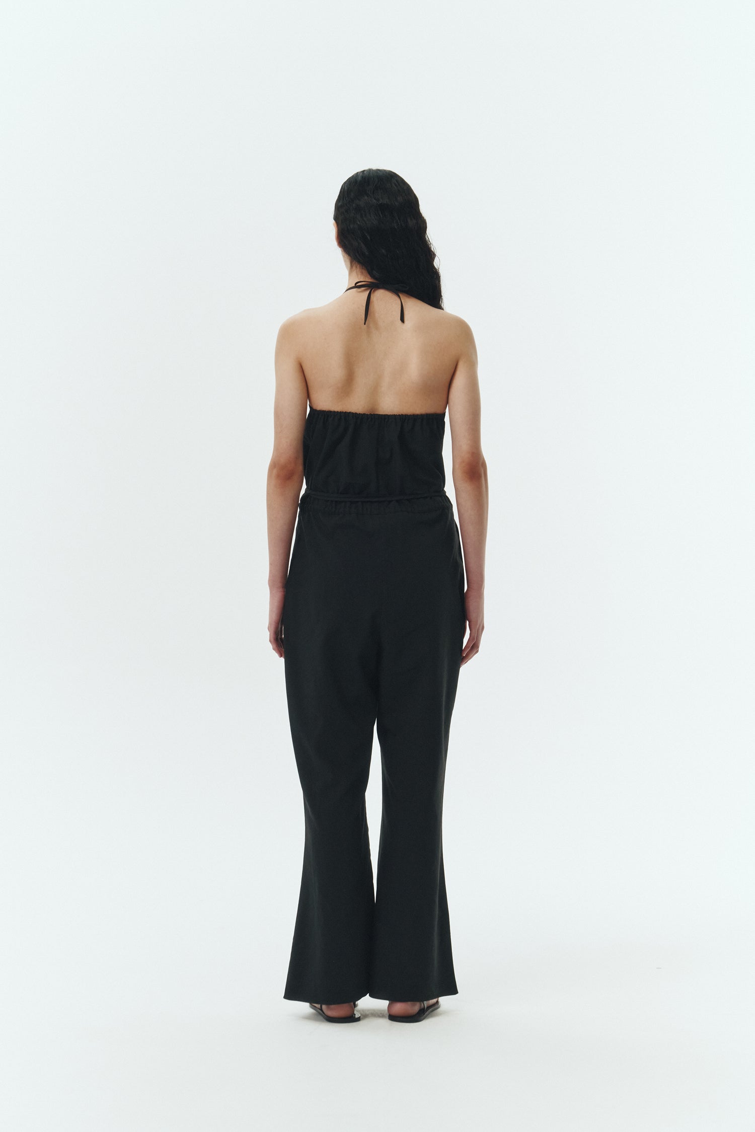 Daisy Jumpsuit in black, sleeveless linen blend jumpsuit with adjustable halterneck, open back, straight-leg silhouette, and relaxed fit.