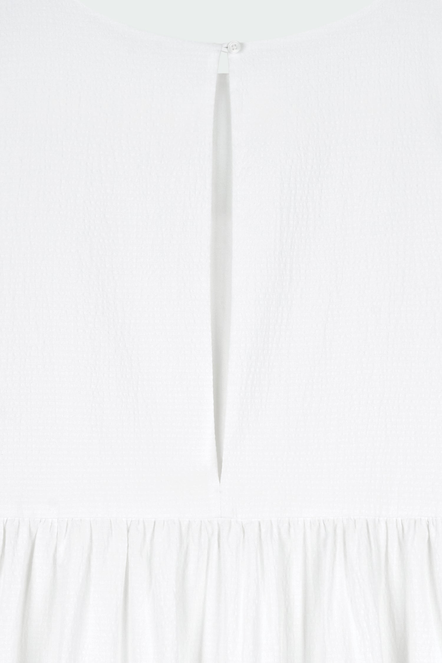 Pina Dress in white a sleeveless midi dress with an open back and button closure, featuring shirring details at the waist and hem, plus hidden side pockets for summer comfort