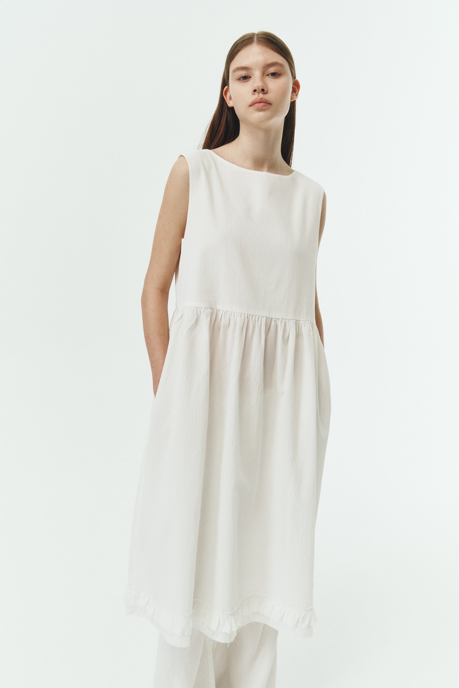 Pina Dress in white a sleeveless midi dress with an open back and button closure, featuring shirring details at the waist and hem, plus hidden side pockets for summer comfort