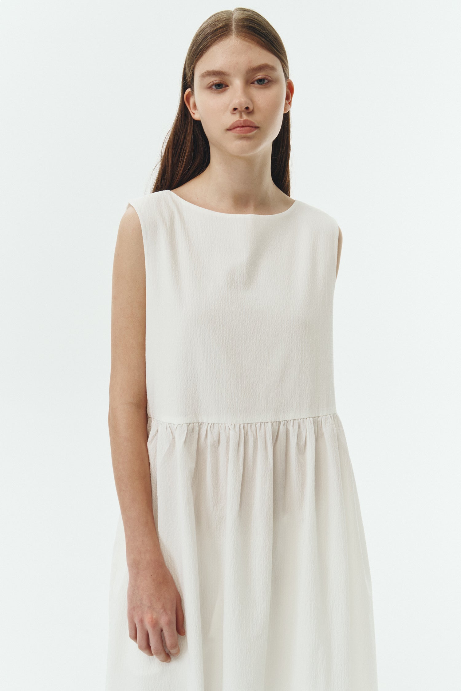 Pina Dress in white a sleeveless midi dress with an open back and button closure, featuring shirring details at the waist and hem, plus hidden side pockets for summer comfort