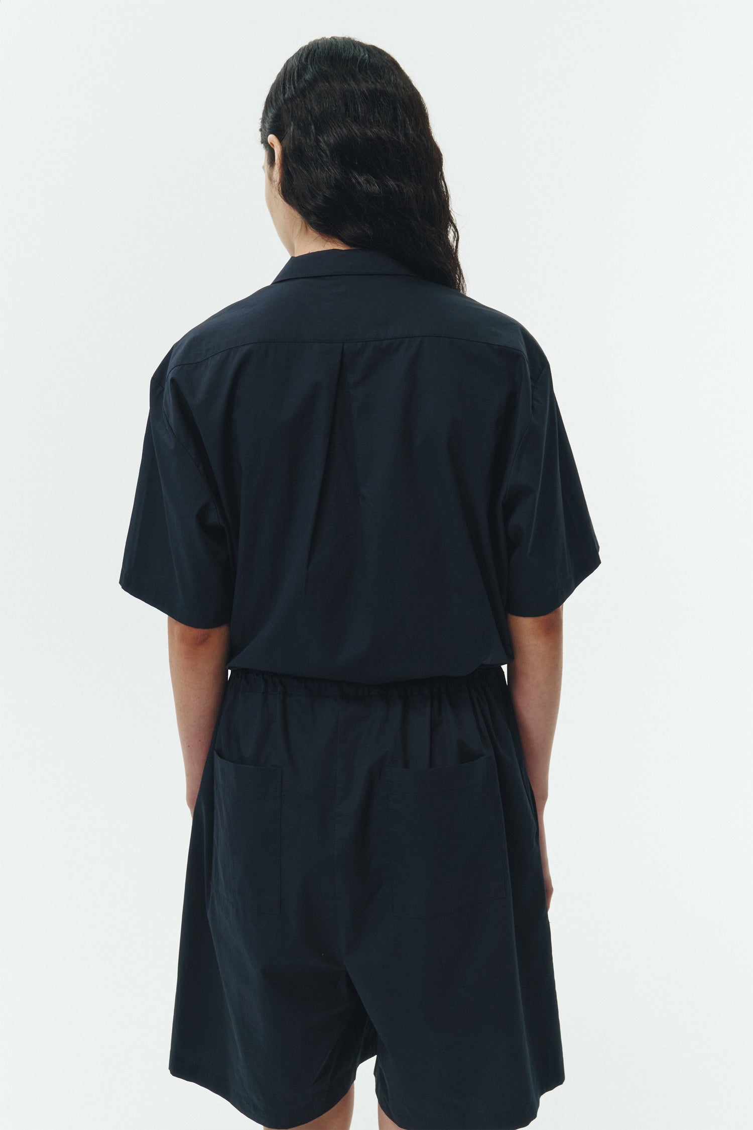 Emma Jumpsuit in navy, short-sleeve cotton jumpsuit with camp collar, front buttons, drawstring waist, and multiple pockets.