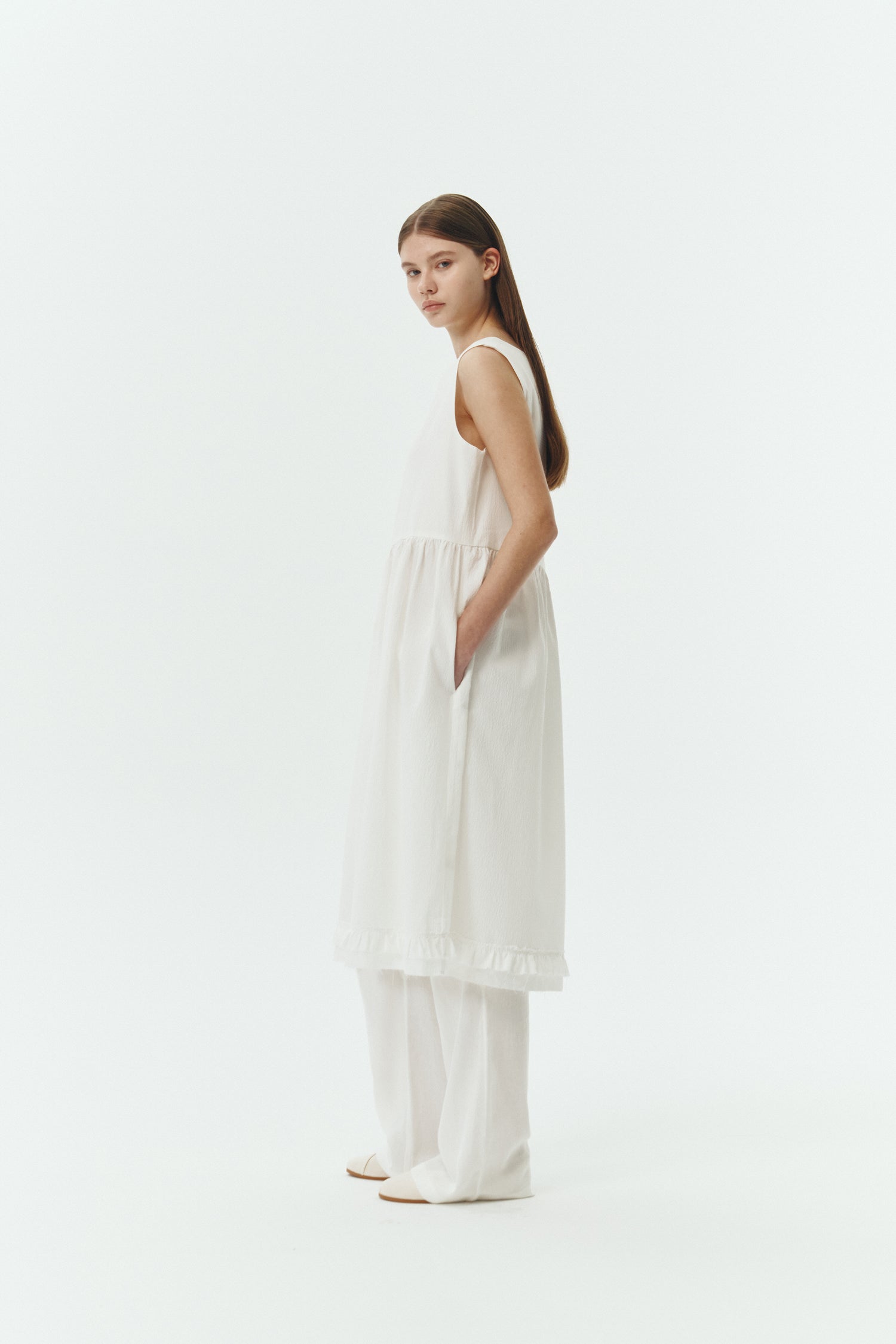 Pina Dress in white a sleeveless midi dress with an open back and button closure, featuring shirring details at the waist and hem, plus hidden side pockets for summer comfort