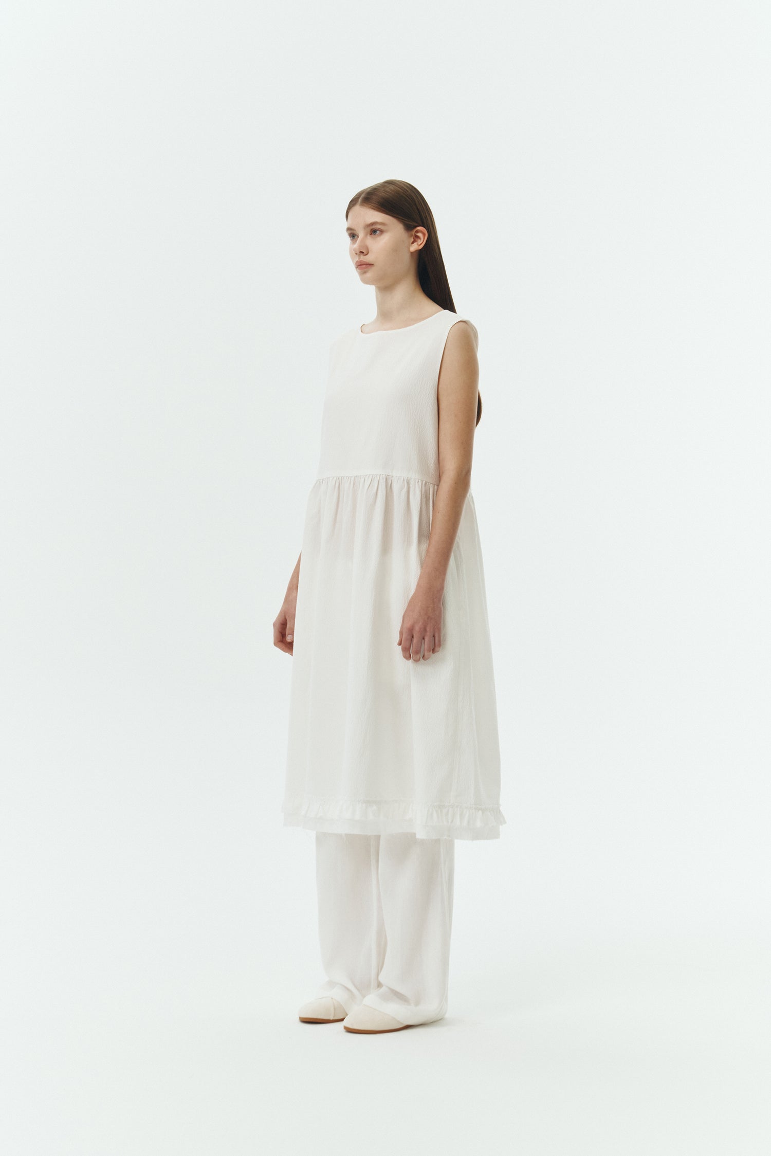 Pina Dress in white a sleeveless midi dress with an open back and button closure, featuring shirring details at the waist and hem, plus hidden side pockets for summer comfort