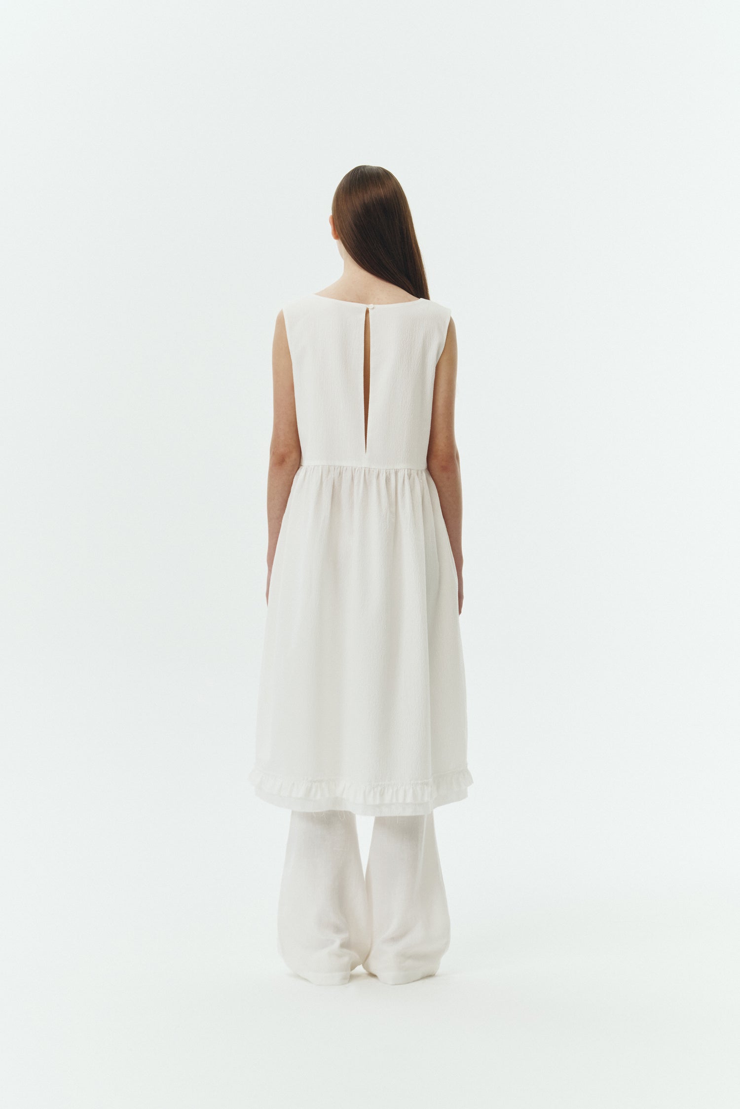 Pina Dress in white a sleeveless midi dress with an open back and button closure, featuring shirring details at the waist and hem, plus hidden side pockets for summer comfort