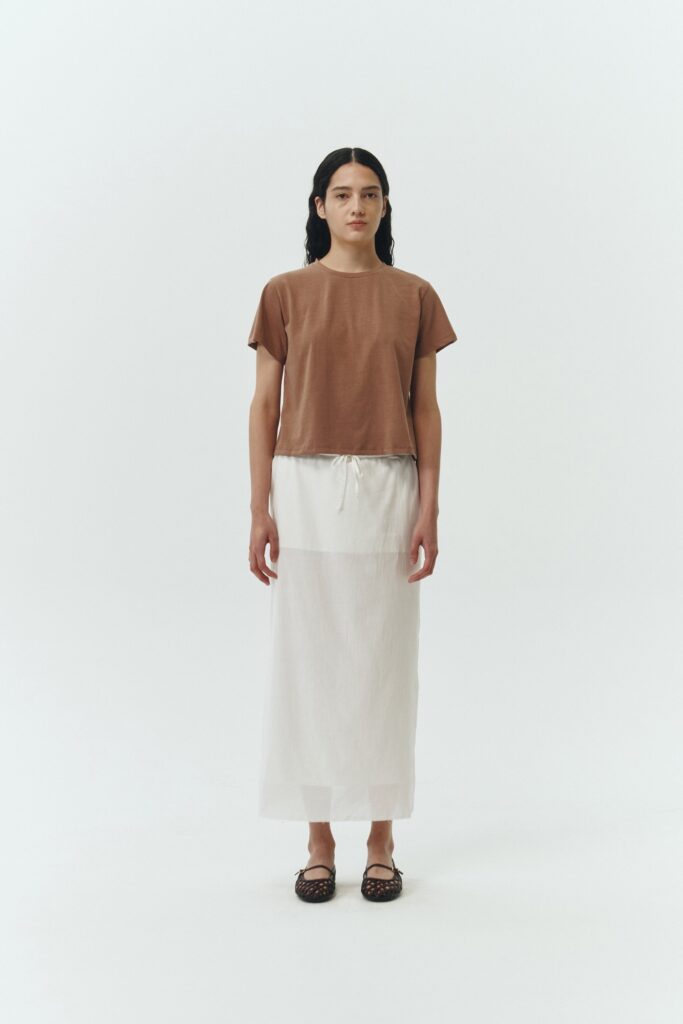 Amelia Skirt in white, a lightweight cotton midi skirt with inner drawstring waist, hidden side pockets, lined layers, raw-edge hem, and a center back slit for ease and movement