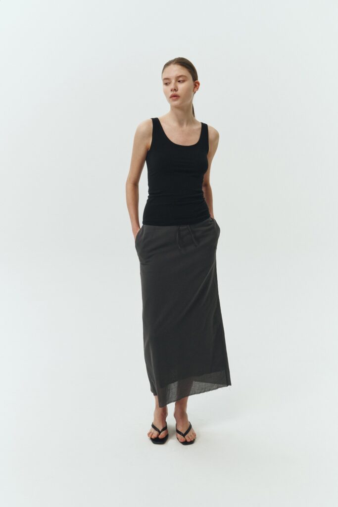 Amelia Skirt in charcoal, a lightweight cotton midi skirt with inner drawstring waist, hidden side pockets, lined layers, raw-edge hem, and a center back slit for ease and movement