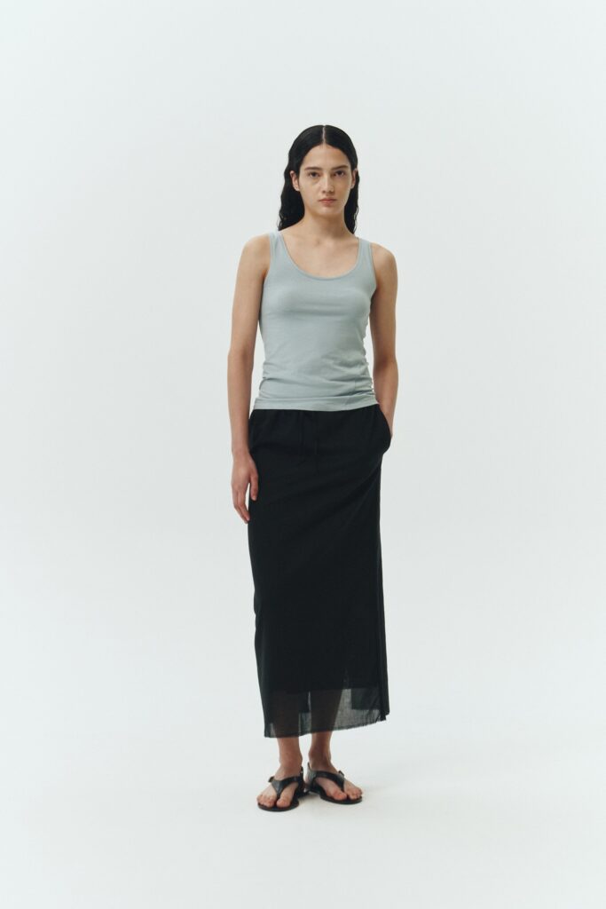 Amelia Skirt in black, a lightweight cotton midi skirt with inner drawstring waist, hidden side pockets, lined layers, raw-edge hem, and a center back slit for ease and movement