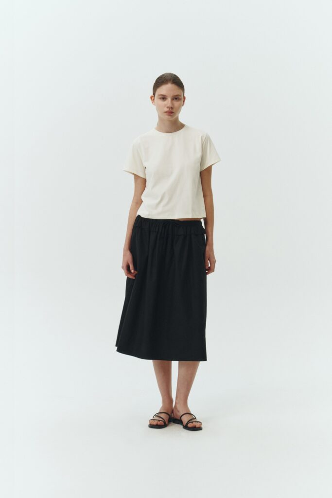 Maryam Skirt in black, a midi cotton skirt with shirred waistband, drawstring detail, side pockets, and a softly flared silhouette
