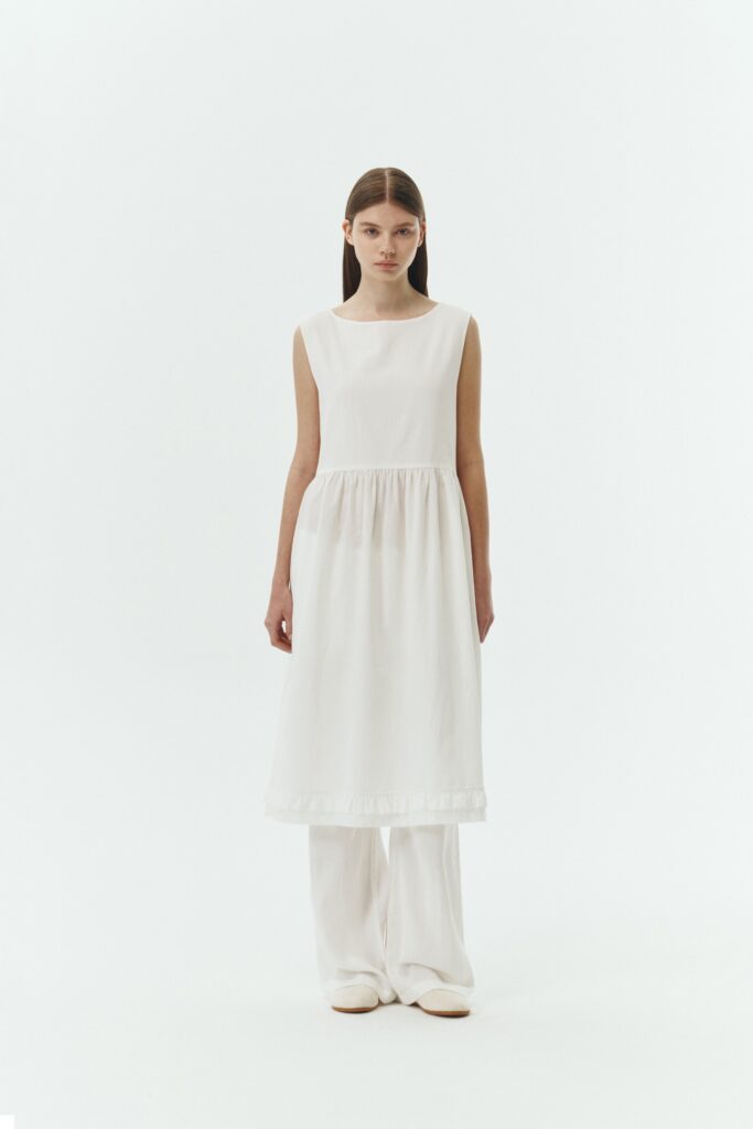 Pina Dress in white a sleeveless midi dress with an open back and button closure, featuring shirring details at the waist and hem, plus hidden side pockets for summer comfort